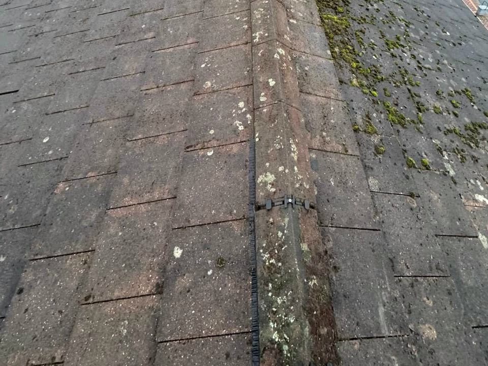 The same roof mid-clean, the left slope cleared of moss and the right slope still covered