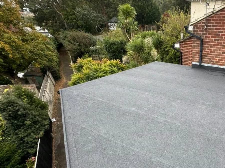 The same flat roof finished in grey mineral felt, flashed in at the brick wall, gardens beyond