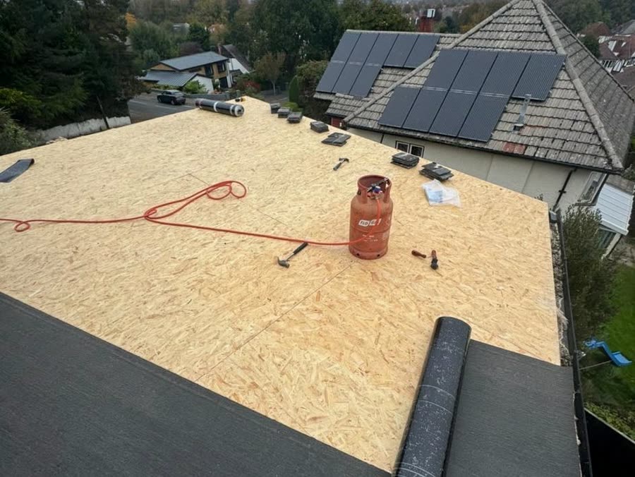 The same flat roof with a new OSB deck down and torch-on felt being rolled out across it