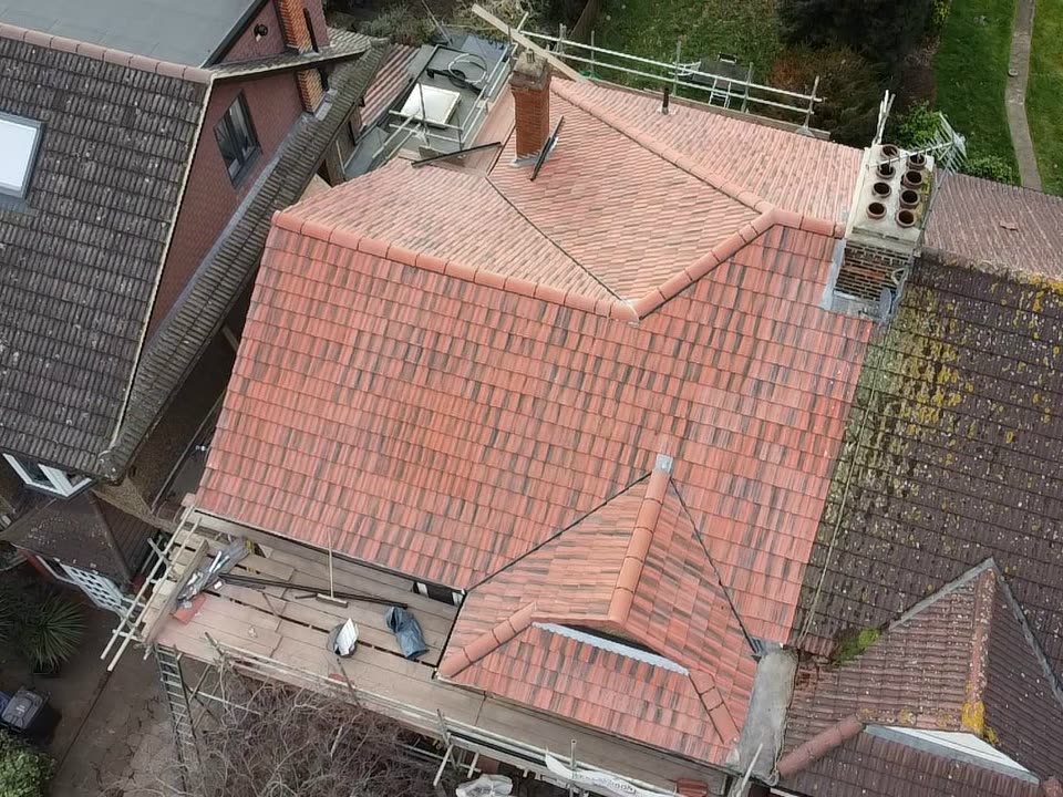 Drone view of the finished roof in new red clay plain tiles, the front gable and chimneys done, scaffolding still up