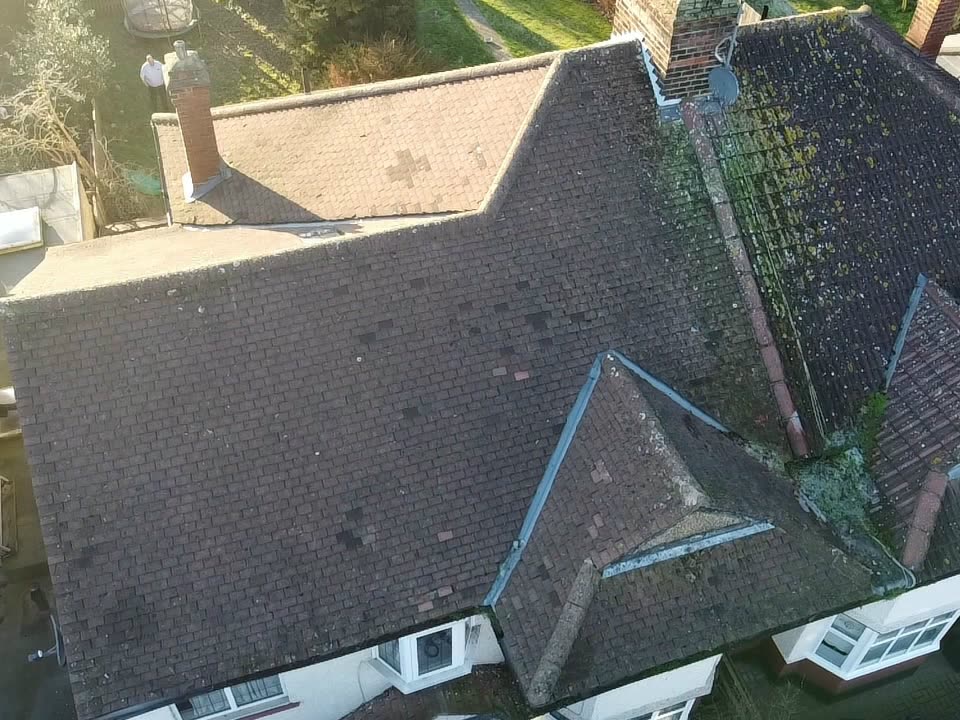 Drone view of an old brown tiled roof with moss, patched tiles and a small front gable, before the re-roof