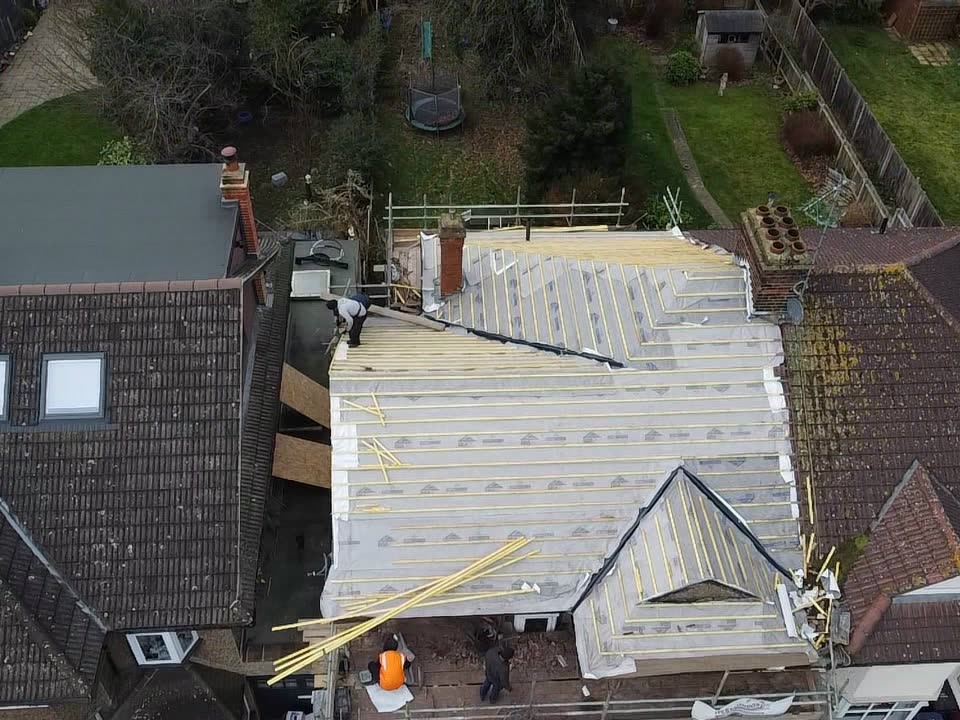 Drone view of the same roof stripped and covered in white breathable membrane with new timber battens, roofers working from the scaffold