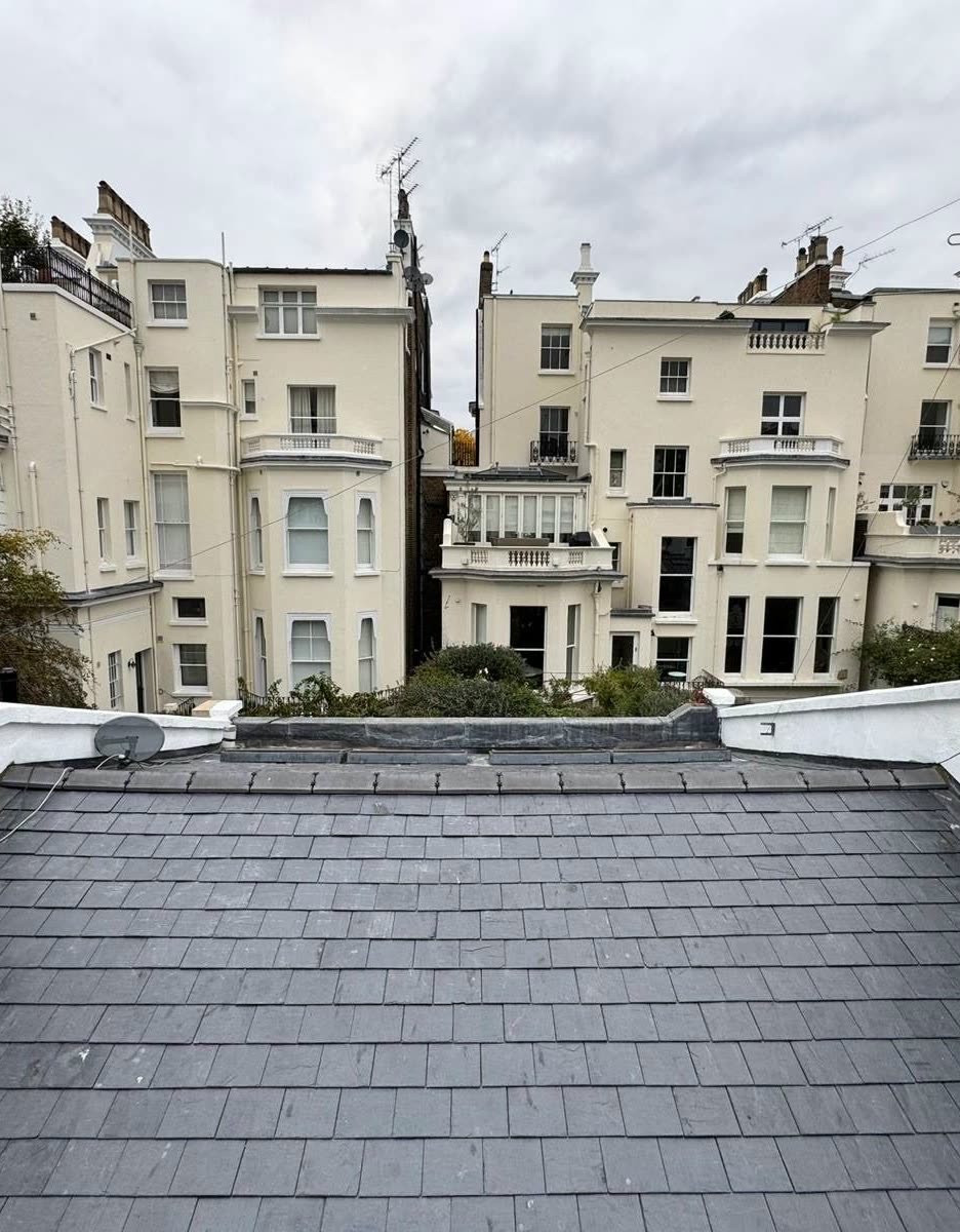 Natural slate roof finished between rendered parapet walls, with a row of cream painted houses behind