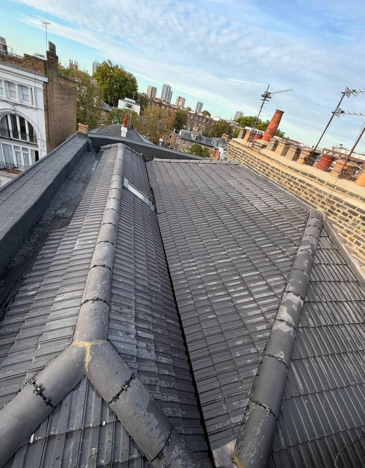 Grey interlocking tiled roof with dry fixed hip and ridge tiles meeting at a central valley