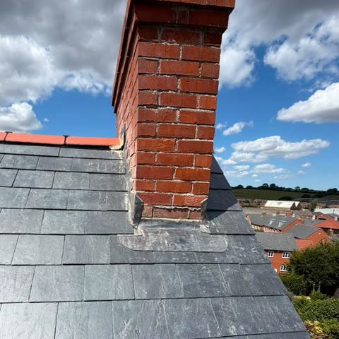 New natural slate roof with red ridge tiles and fresh lead flashing around a brick chimney