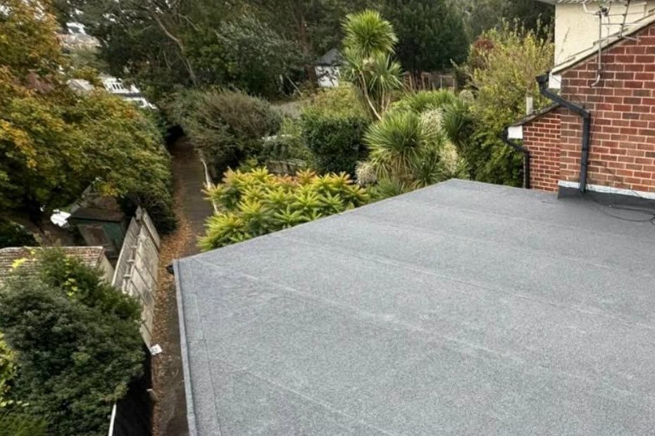 Finished grey mineral felt flat roof on a rear extension, flashed in at the brick wall, gardens beyond