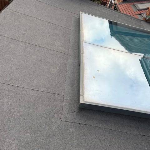 New grey mineral felt flat roof with a large flat glass rooflight, seen from above