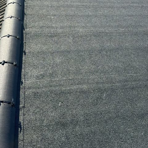 Finished grey mineral felt flat roof running up to a clipped ridge roll along one side