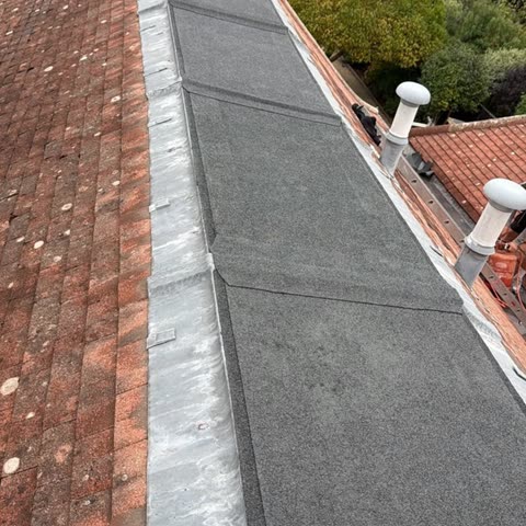 New mineral felt flat roof section with lead flashings running between two red tiled pitched roofs