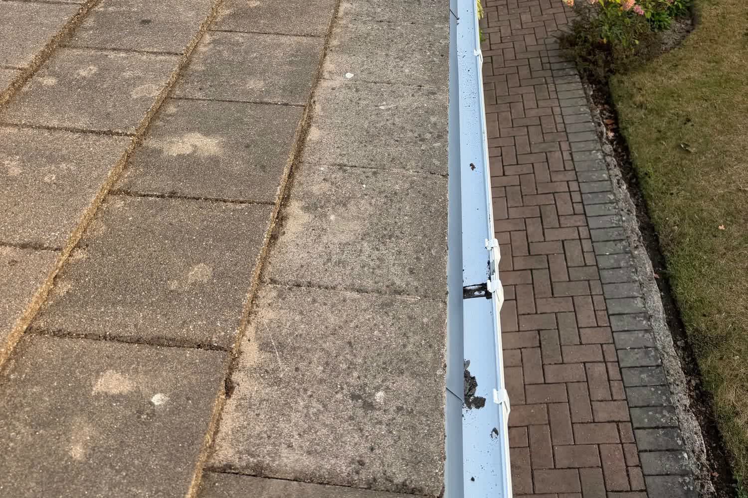 Cleared white gutter along the eaves of a tiled roof above a paved garden