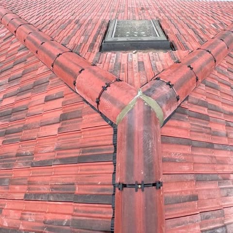 Newly tiled hip roof seen from the ridge, dry-fix hip and ridge tiles meeting around a roof window