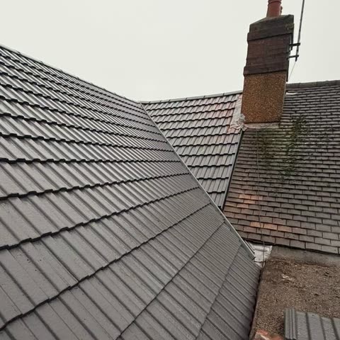 New grey tiled roof slope meeting the existing roof by a chimney