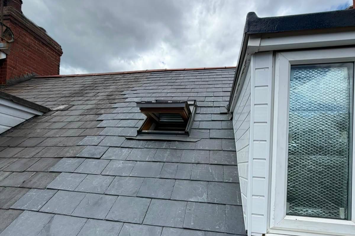 Section of slate roof replaced around a roof window beside a dormer, new slates next to the old