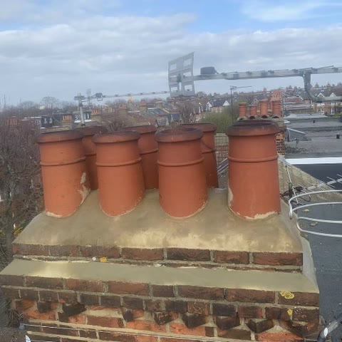 Brick chimney stack with eight terracotta pots set in new sand and cement flaunching, rooftops across Ealing behind