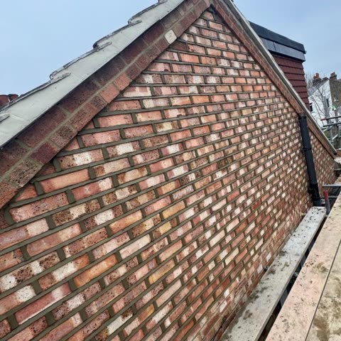 Gable end rebuilt in reclaimed-look red brick with a new mortared verge, the scaffold alongside
